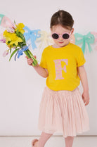 a 3 year old girl wearing a personalised kids yellow t-shirt with an initial cut from sadie rose liberty floral print on the front