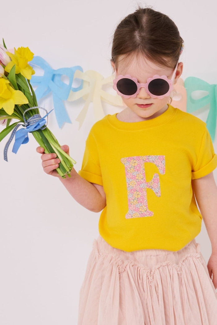 a 3 year old girl wearing a personalised kids yellow t-shirt with an initial cut from sadie rose liberty floral print on the front