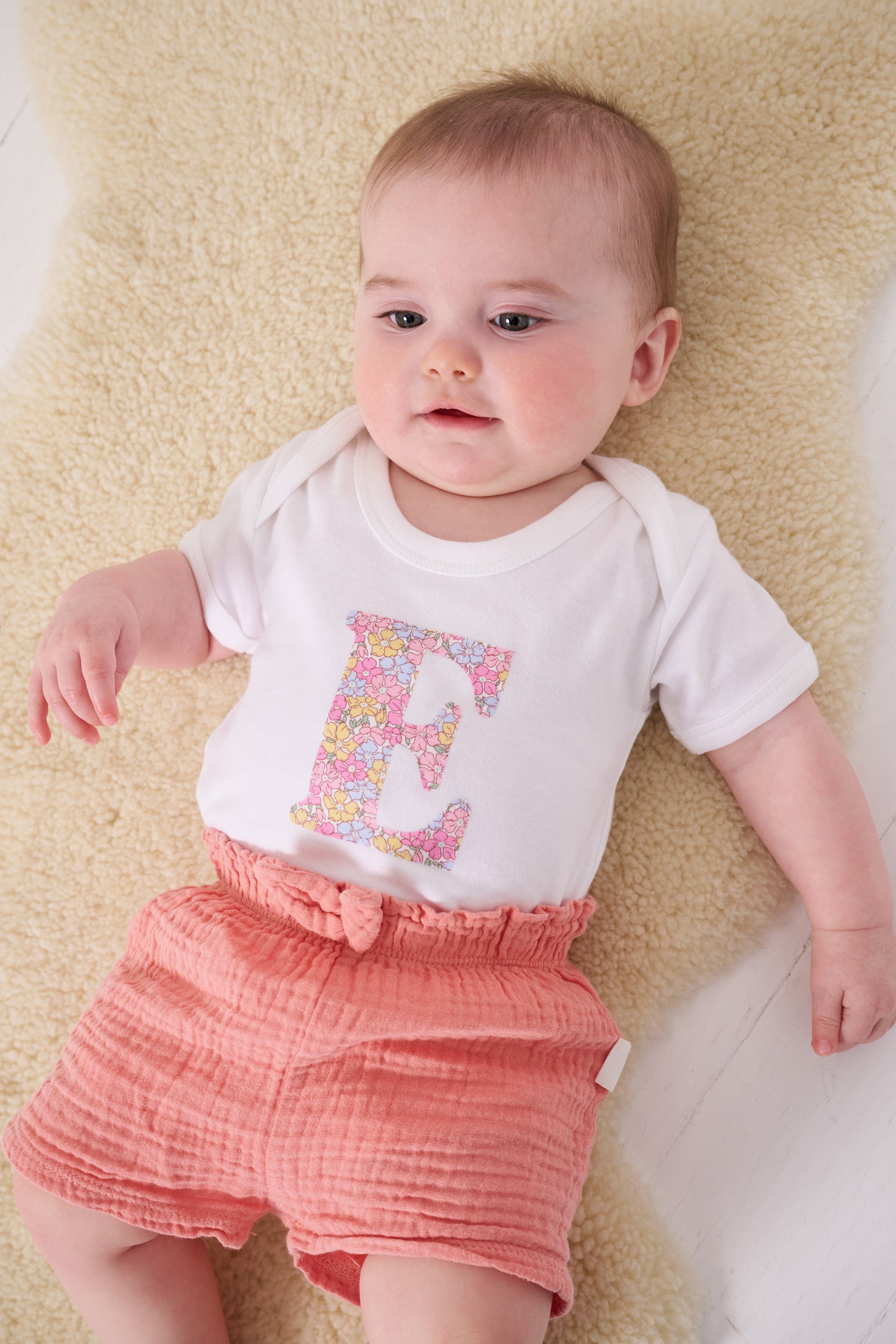 a 6 month old baby wearing a personalised bodysuit baby grow with her initial cut from floral sadie rose Liberty print 