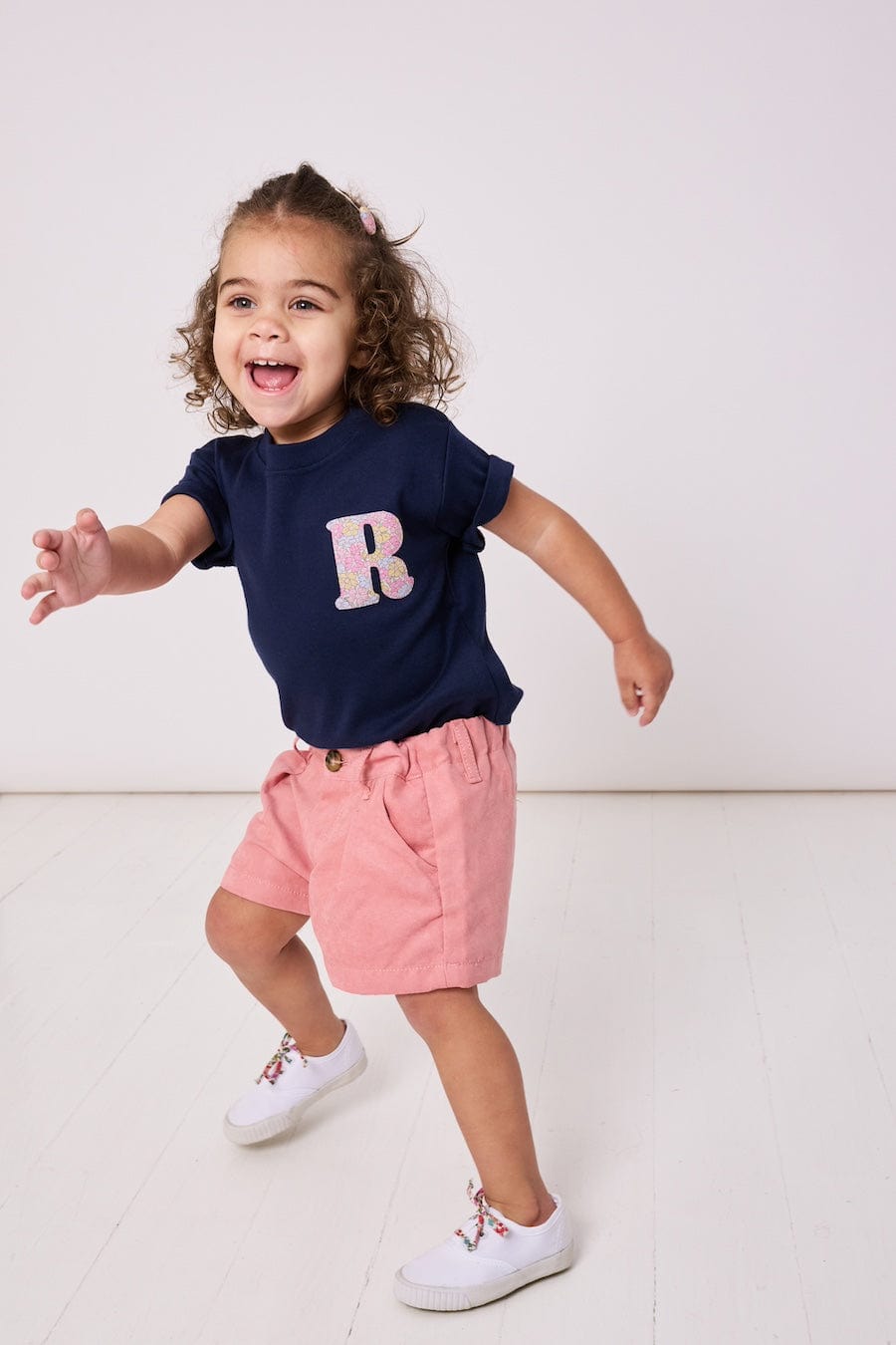 A smiling 2 year old girl wearing a personalised kids cotton t-shirt with a Liberty print initial on the front.
