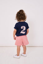 A 2 year old girl wearing a kids cotton t-shirt with a Liberty print number 2 on the back.