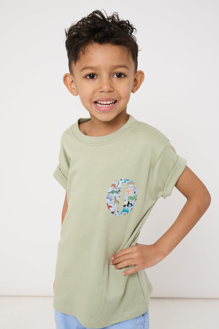 a 4 year old boy wearing a sage green t-shirt with a small initial on the front cut from zoo animal Liberty print