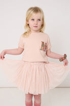 A 4 year old girl wearing a pale pink t-shirt with a Liberty Nell Annie and May floral small initial on the front
