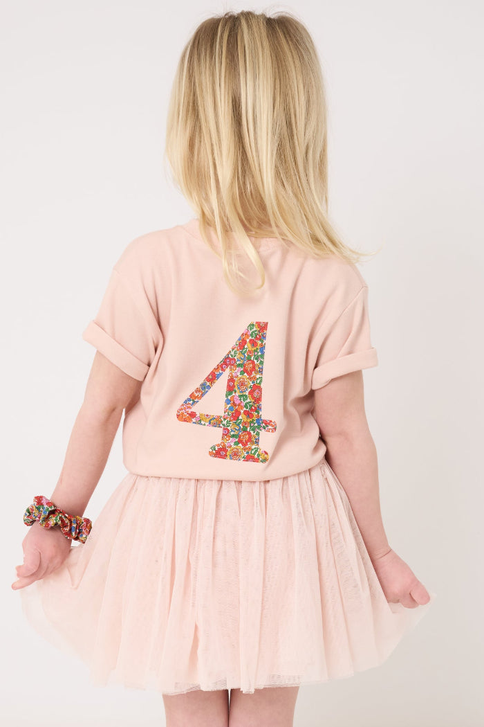 A 4 year old girl wearing a pale pink t-shirt with a Liberty Nell Annie and May floral small initial on the front
