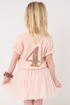 A 4 year old girl wearing a pale pink t-shirt with a Liberty Nell Annie and May floral small initial on the front