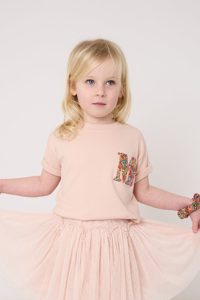 Young girl wearing a pink outfit with a skirt and t-shirt, standing against a white background