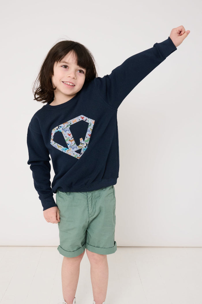 Child wearing a personalised navy blue sweatshirt with an initial superhero logo on the front in Quey 2 animal liberty print