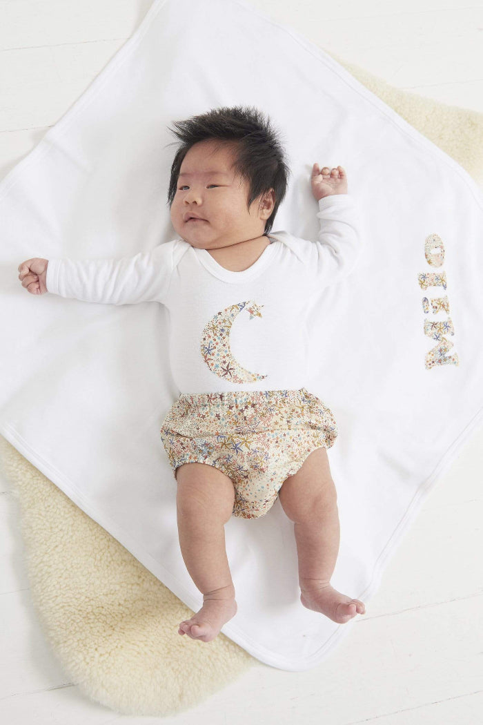 A new baby in a white cotton babygrow with a moon and hanging star sewn on the front, cut from Adelajda starry Liberty print.