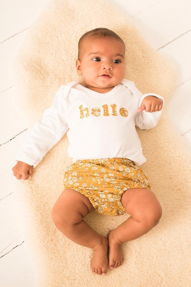Magnificent Stanley Bodysuit 'hello' Bodysuit in choice of Liberty Print Magnificent Stanley Bodysuit 'hello' Bodysuit. New baby wears a white bodysuit with the word hello on it. the letters are cut from a mustard capel floral liberty print 