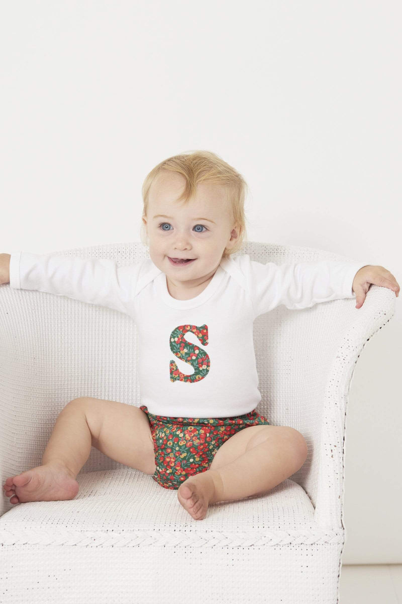 A smiling baby wearing a personalised initial Magnificent Stanley baby Bodysuit in Glitter Wiltshire Liberty Print