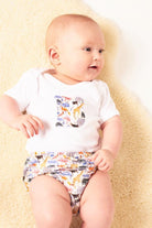 A 3 month old baby wearing a personalised white cotton baby bodysuit with his initial on the front, cut from Queue for the Zoo Liberty print featuring zoo animals.