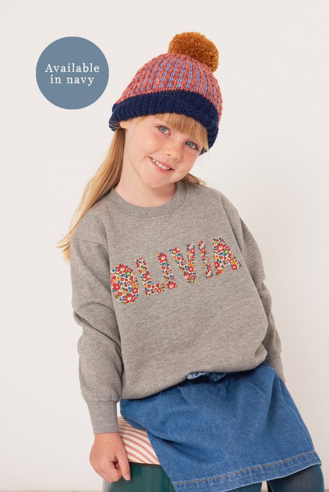 a smiling 5 year old girl wearing a grey kids personalised sweatshirt with her name on it cut from Betsy Ann Liberty print.







