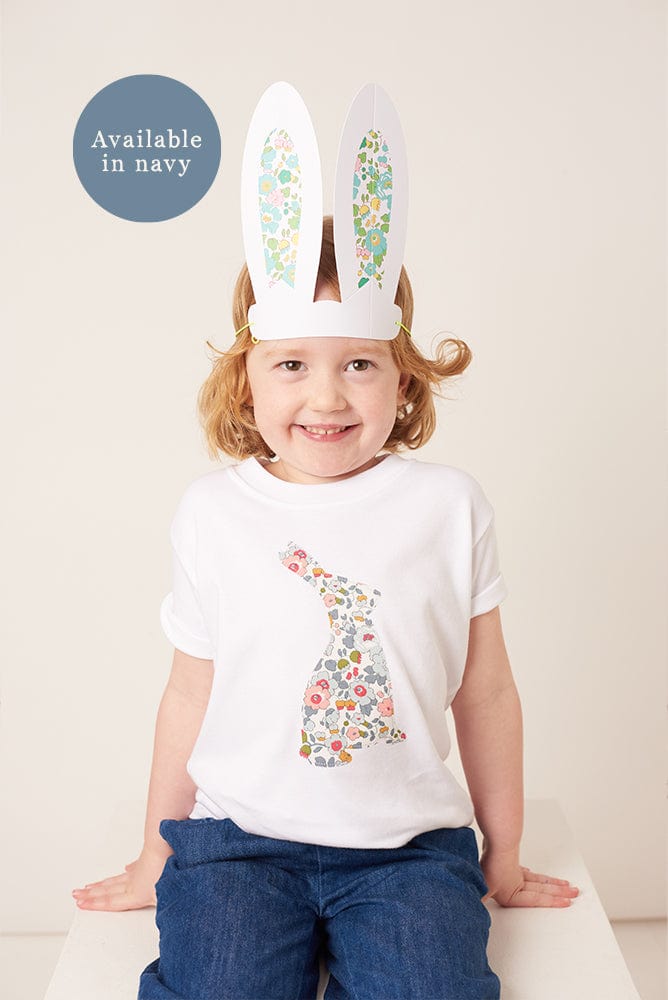 A smiling girl wearing a white cotton t-shirt with a floral liberty print bunny on the front and she has liberty betsy bunny ears on her head.
