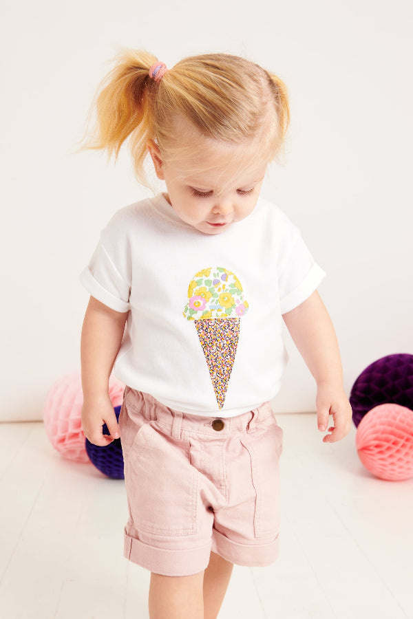 A little girl wearing a white cotton summer t-shirt with a liberty floral ice cream sewn on the front