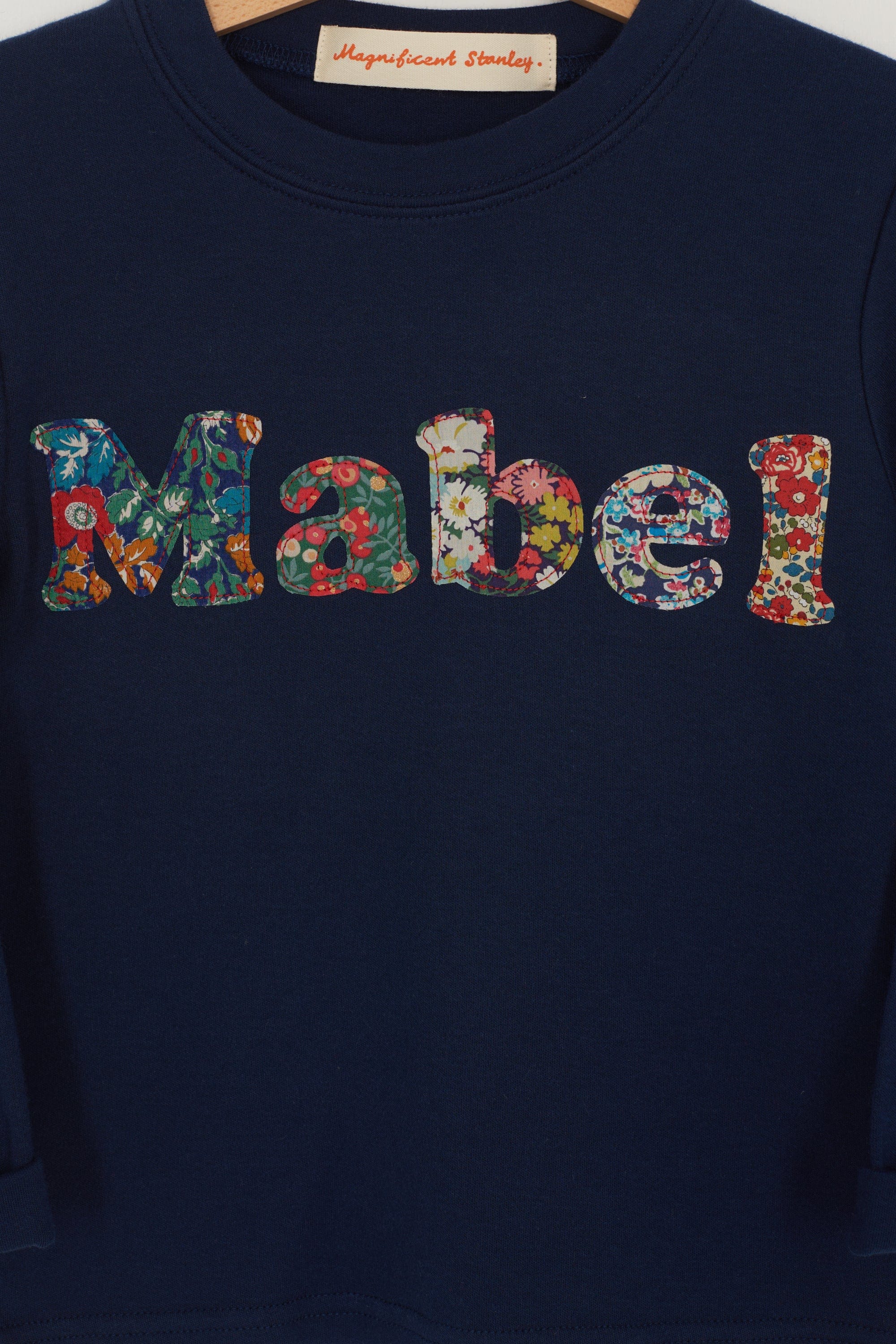 A navy t-shirt with the name mabel  sewn on in mixed Liberty print lowercase letters.