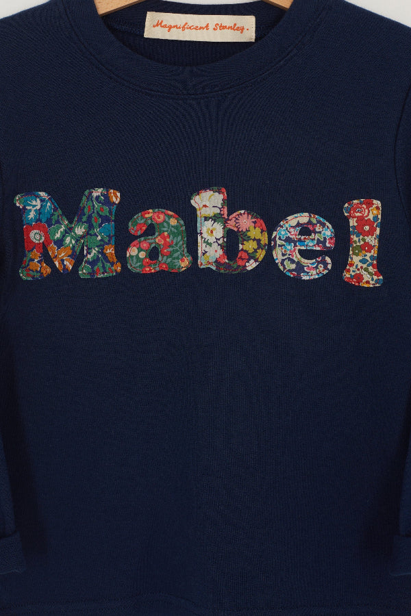 A navy t-shirt with the name mabel  sewn on in mixed Liberty print lowercase letters.