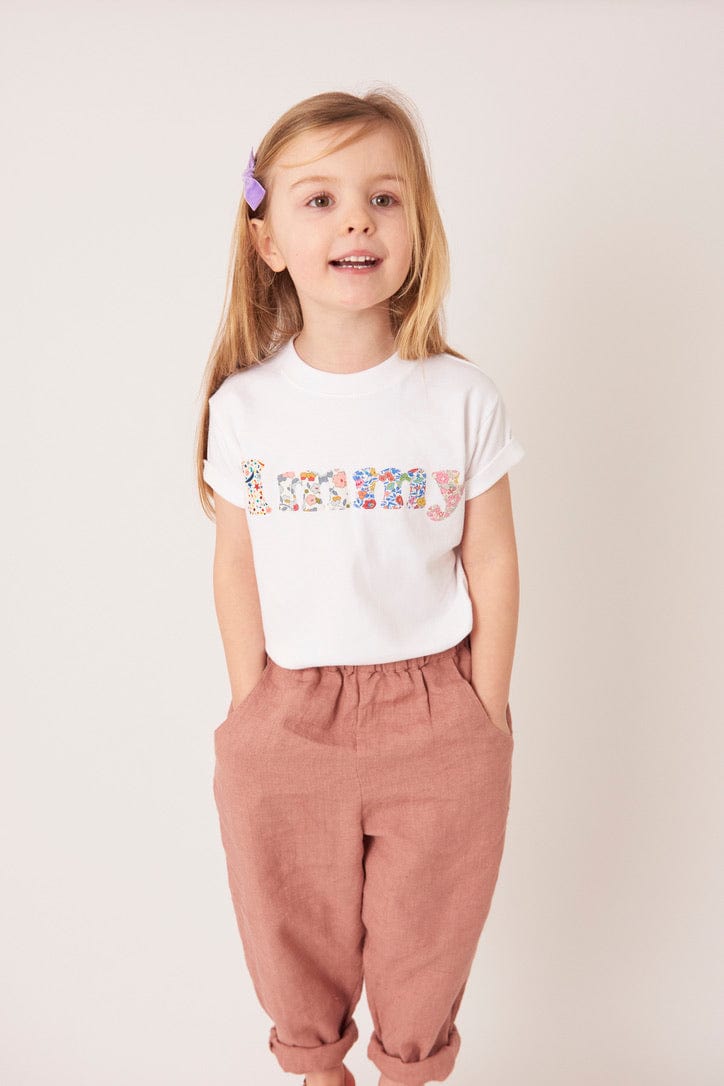 A 5 year old girl wears a personalised white t-shirt with her name on in a mix of Liberty prints.