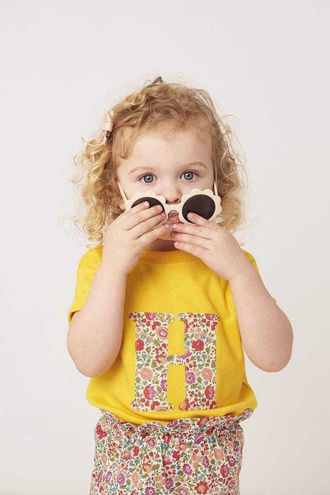 a smiling 2 year old girl wearing a personalised kids yellow t-shirt with an initial cut from d'anjo liberty floral print on the front