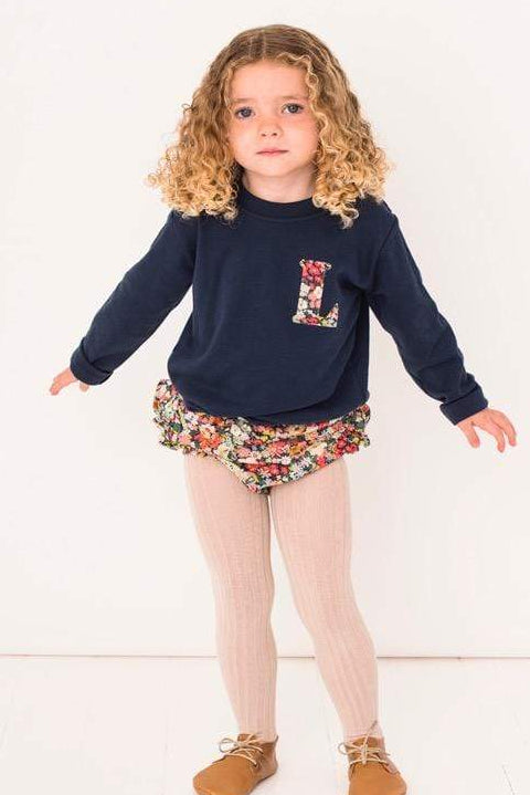 A 2 year old girl wearing a navy cotton tee with a small initial on the front in a floral Liberty fabric.